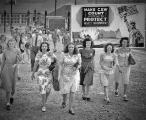 Shift change at the Y-12 uranium enrichment facility in Oak Ridge, Tennessee, during the Manhattan Project. Notice the billboard: "Make CEW count — Continue to protect project information."